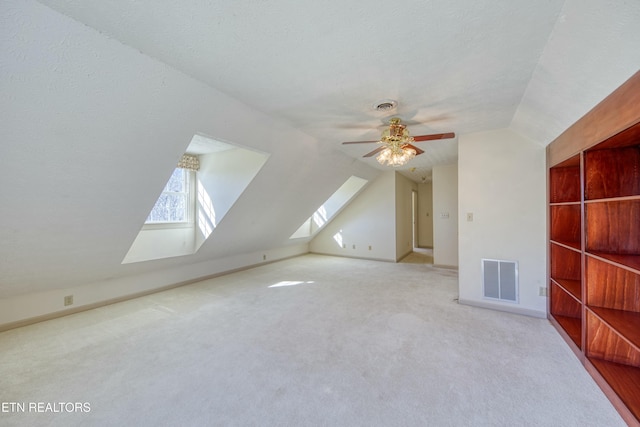 additional living space with ceiling fan, light carpet, vaulted ceiling with skylight, and a textured ceiling