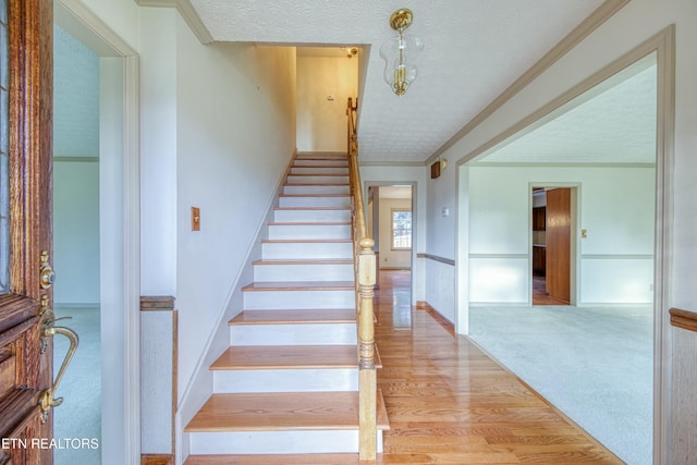 stairs with crown molding, carpet flooring, and a textured ceiling