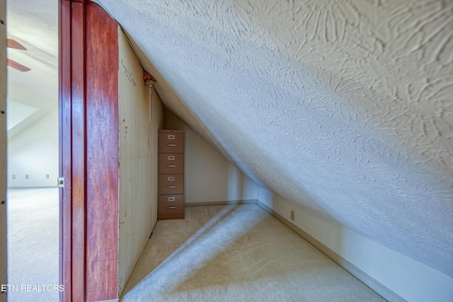 additional living space with ceiling fan, vaulted ceiling, light colored carpet, and a textured ceiling