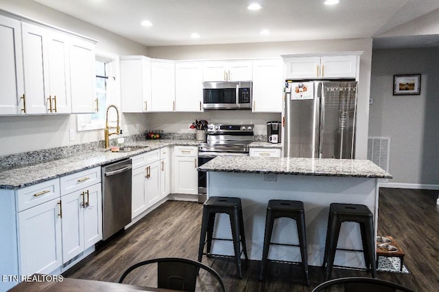 kitchen with a kitchen bar, sink, white cabinetry, a center island, and stainless steel appliances