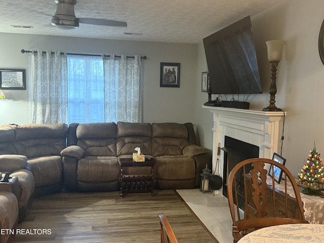 living room with hardwood / wood-style floors, a tile fireplace, a textured ceiling, and ceiling fan