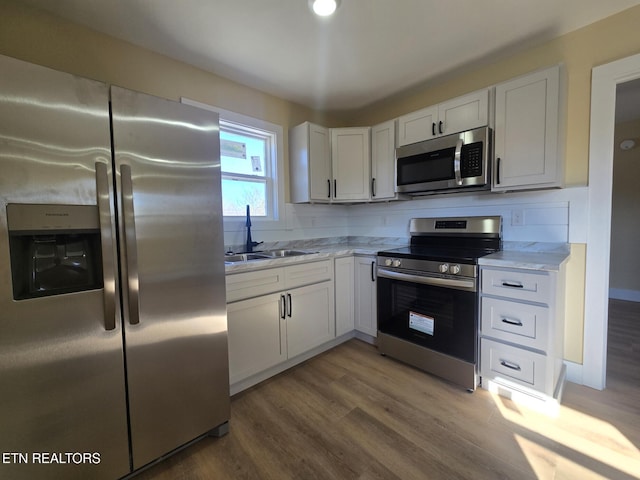 kitchen featuring white cabinets, wood finished floors, light stone countertops, stainless steel appliances, and a sink