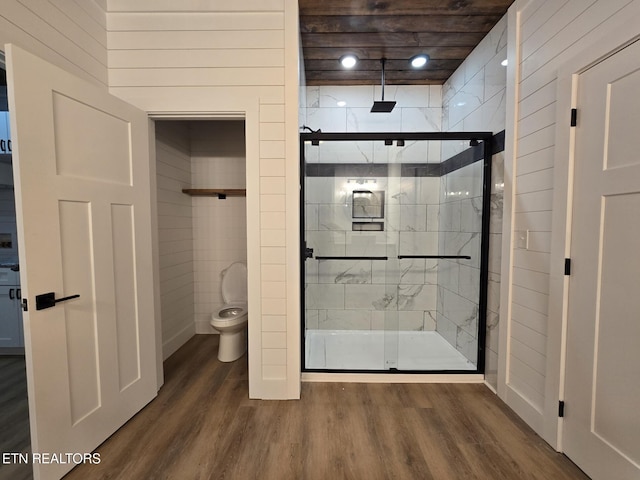 bathroom with toilet, a shower stall, wooden walls, and wood finished floors