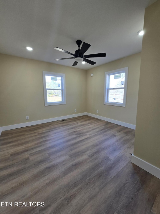 empty room featuring a ceiling fan, a wealth of natural light, dark wood finished floors, and baseboards