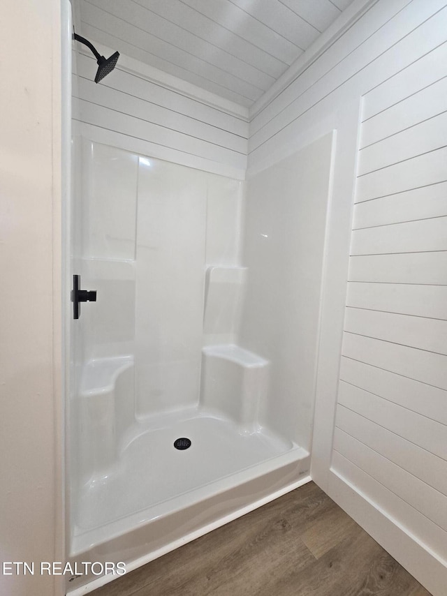 bathroom with a stall shower, wood finished floors, and wood walls