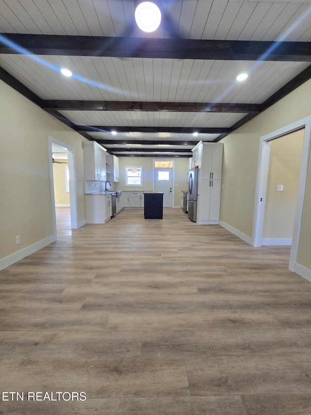 unfurnished living room with light wood-type flooring, a sink, beamed ceiling, and baseboards