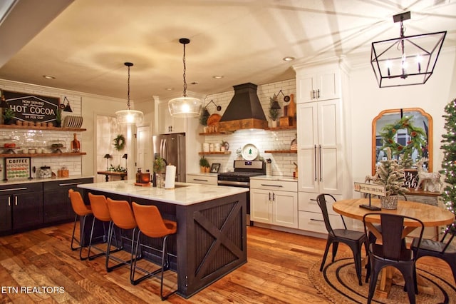 kitchen with appliances with stainless steel finishes, a center island with sink, light stone countertops, white cabinets, and custom exhaust hood