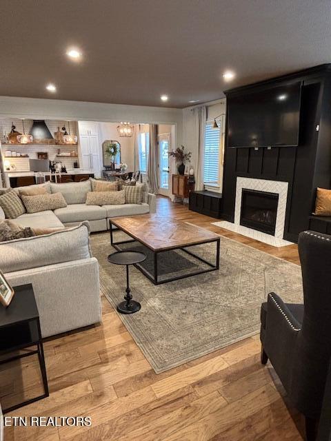 living room featuring a tiled fireplace, a notable chandelier, and light hardwood / wood-style floors