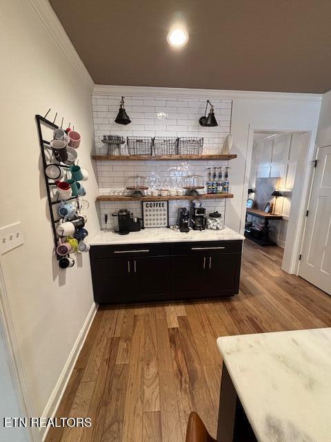 bar featuring decorative backsplash, crown molding, and light hardwood / wood-style flooring