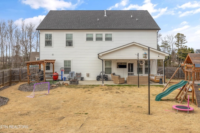 rear view of property featuring a playground, a shingled roof, a fenced backyard, an outdoor living space with a fire pit, and a patio