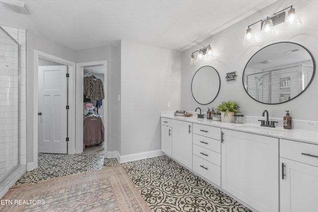 full bathroom featuring a tile shower, double vanity, a sink, a walk in closet, and baseboards