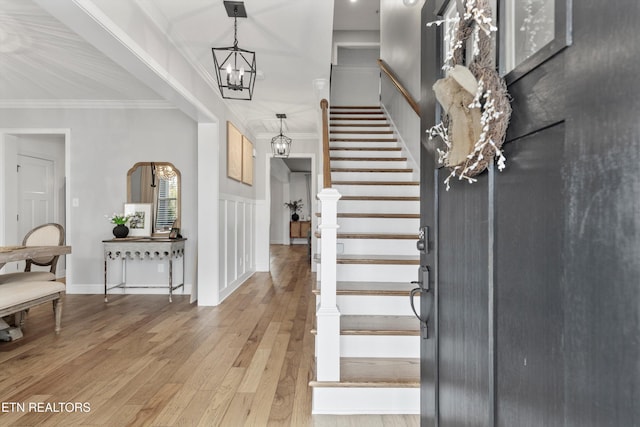 entrance foyer with stairway, an inviting chandelier, ornamental molding, and light wood-type flooring