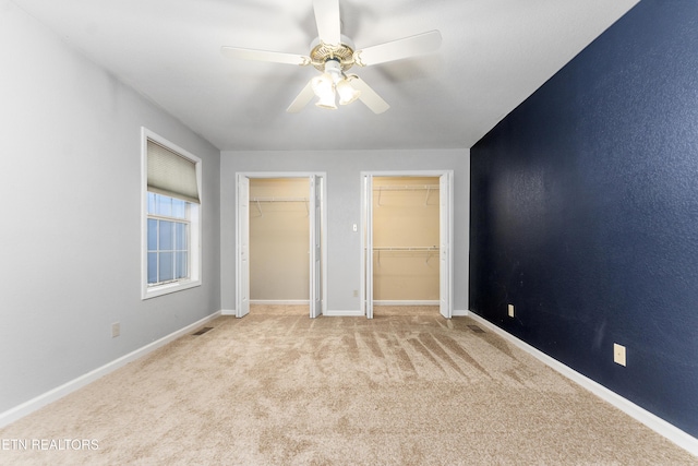 unfurnished bedroom with multiple closets, light colored carpet, and ceiling fan