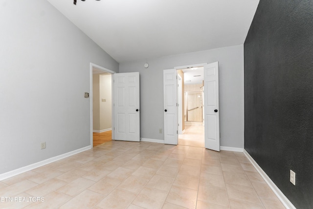 unfurnished bedroom with ensuite bath, lofted ceiling, and light tile patterned floors