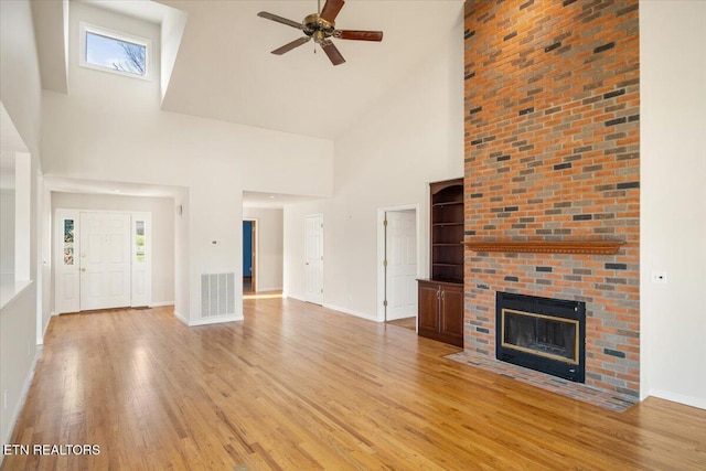 unfurnished living room featuring a brick fireplace, visible vents, light wood finished floors, and ceiling fan