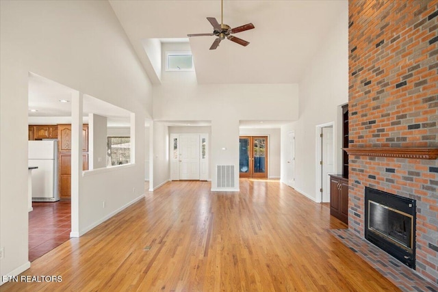 unfurnished living room featuring visible vents, a brick fireplace, baseboards, light wood-style floors, and a ceiling fan