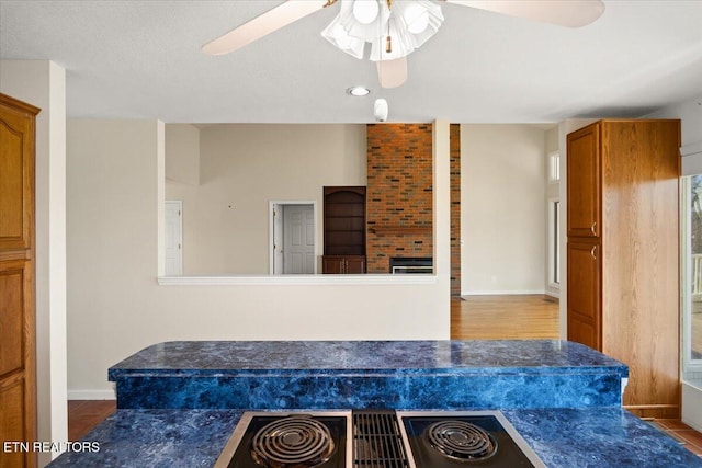 interior space with brown cabinets, dark countertops, stovetop with downdraft, baseboards, and ceiling fan