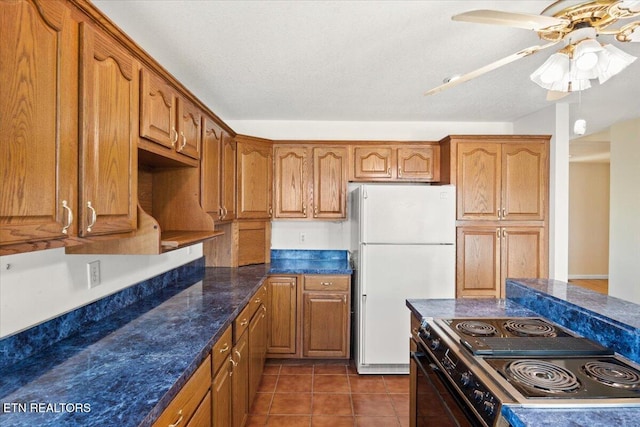 kitchen featuring brown cabinetry, range with electric stovetop, dark tile patterned flooring, and freestanding refrigerator