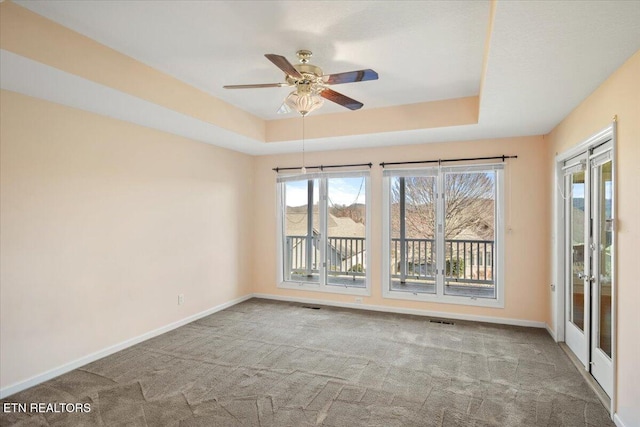 carpeted empty room with baseboards, a raised ceiling, visible vents, and a ceiling fan