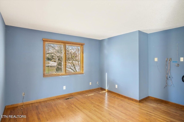 spare room featuring wood finished floors, visible vents, and baseboards