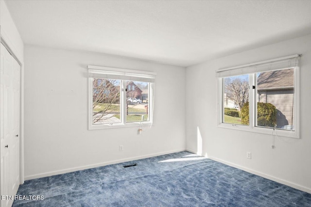 unfurnished bedroom featuring carpet flooring, multiple windows, baseboards, and visible vents