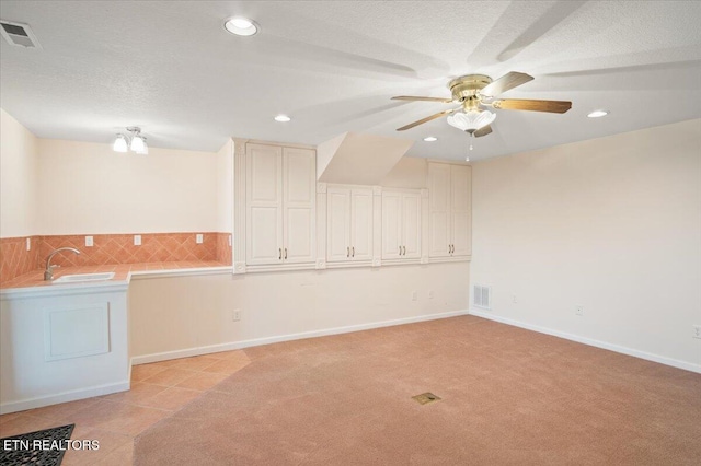 unfurnished room with visible vents, light colored carpet, a textured ceiling, and a sink