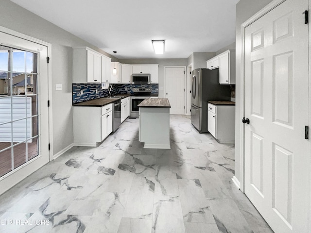 kitchen featuring white cabinetry, appliances with stainless steel finishes, a kitchen island, pendant lighting, and decorative backsplash