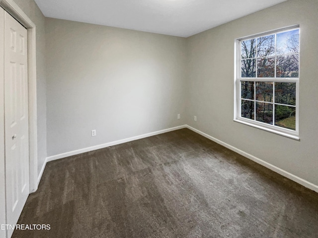 unfurnished bedroom with a closet, dark carpet, and multiple windows