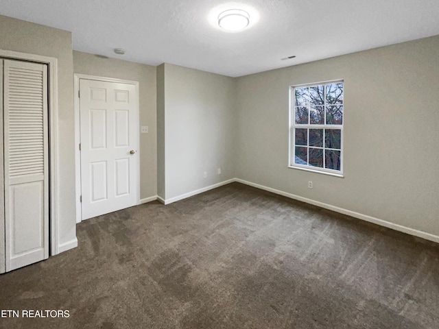 unfurnished bedroom with dark carpet and a closet