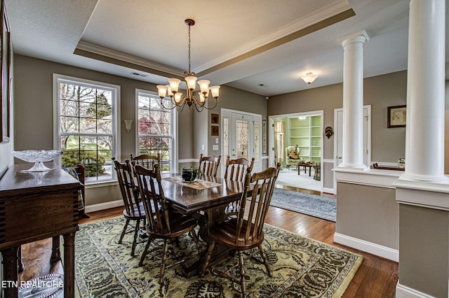dining room with crown molding, dark wood-type flooring, decorative columns, and a raised ceiling
