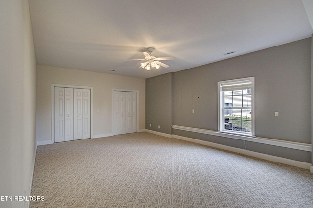 unfurnished bedroom featuring multiple closets, ceiling fan, and carpet flooring