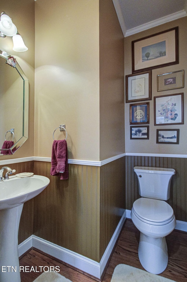 bathroom with toilet, sink, crown molding, wooden walls, and hardwood / wood-style floors