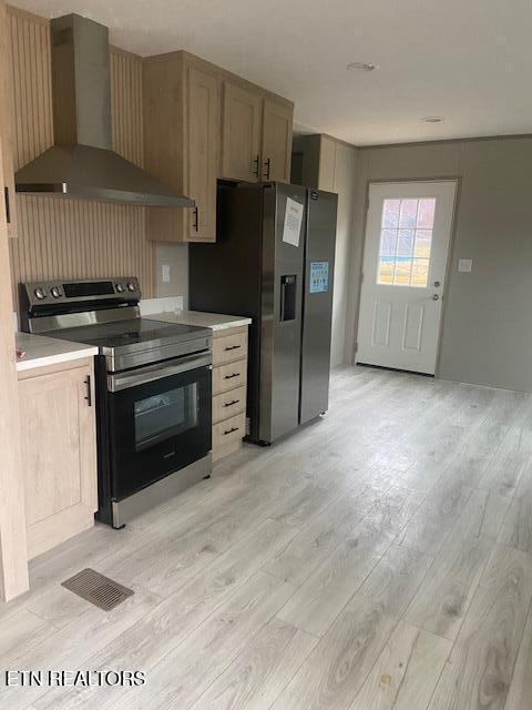 kitchen featuring stainless steel appliances, light wood-type flooring, and wall chimney range hood