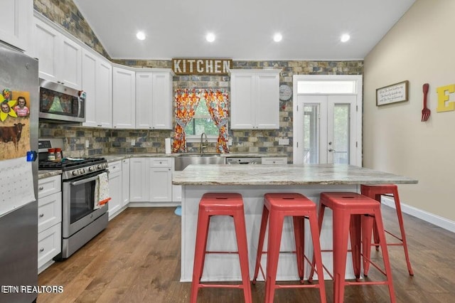 kitchen with a breakfast bar, white cabinetry, stainless steel appliances, a center island, and light stone counters