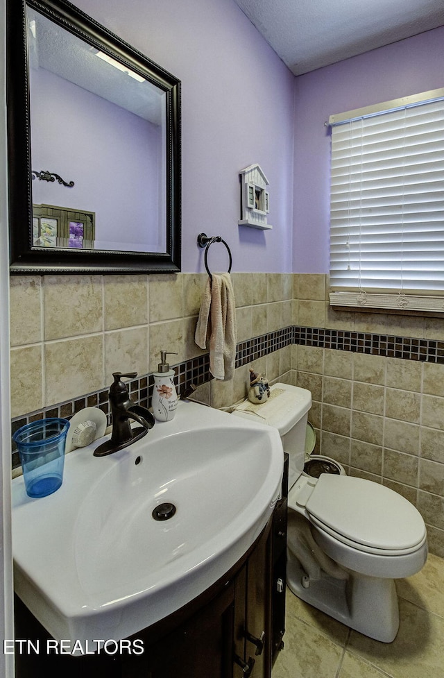 half bath with tile patterned floors, vanity, toilet, and tile walls