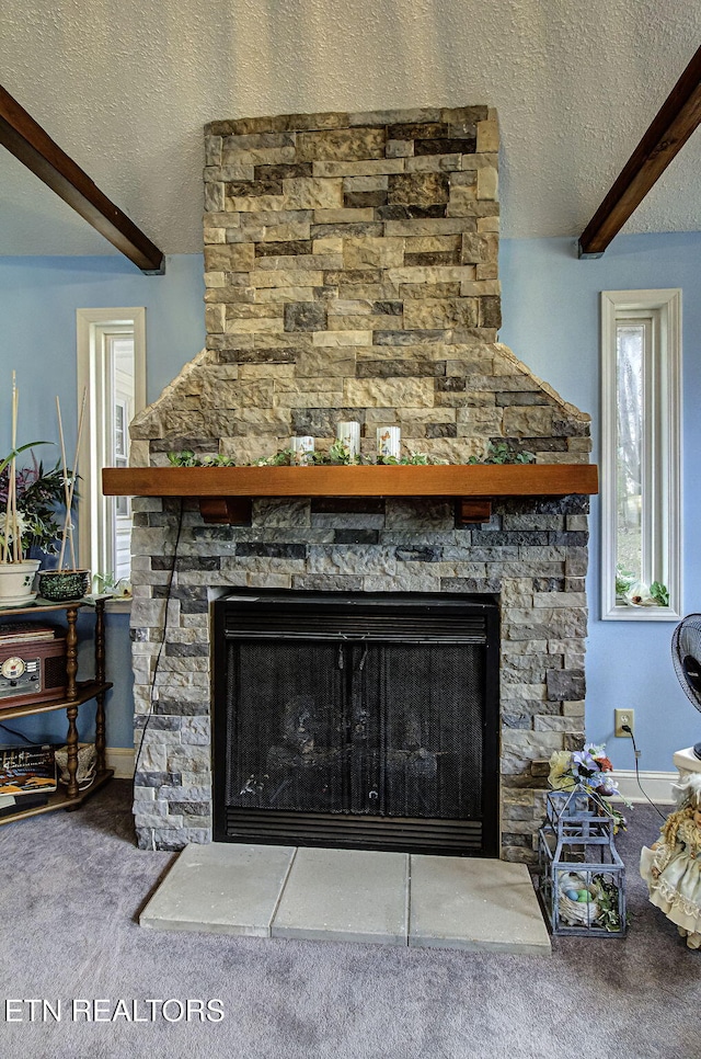 interior details featuring beam ceiling, a textured ceiling, a stone fireplace, and carpet flooring