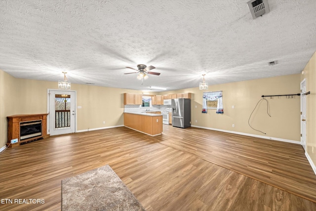 unfurnished living room featuring ceiling fan with notable chandelier, light hardwood / wood-style flooring, and a textured ceiling