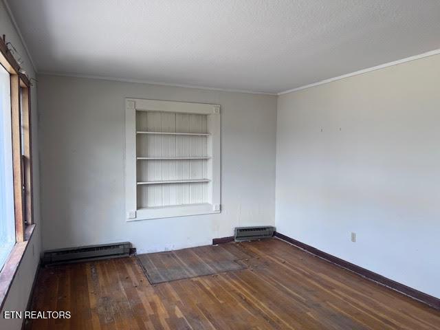 empty room featuring built in shelves, crown molding, baseboard heating, plenty of natural light, and dark hardwood / wood-style floors