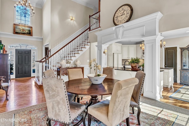 dining space featuring light wood-type flooring, ornamental molding, a chandelier, and a high ceiling