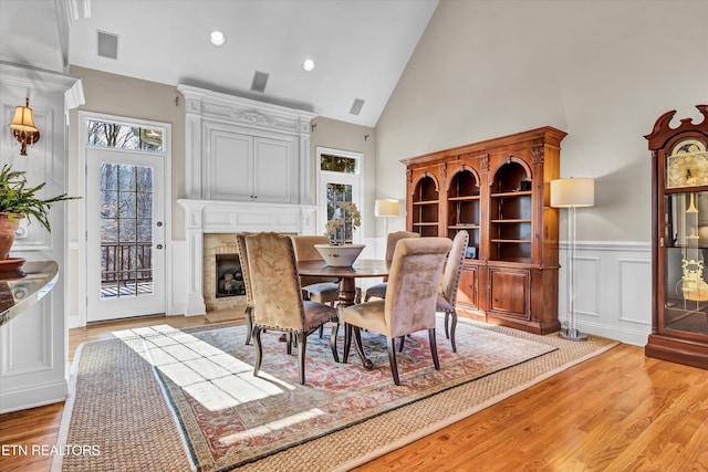 dining room with light hardwood / wood-style flooring, high vaulted ceiling, and a large fireplace