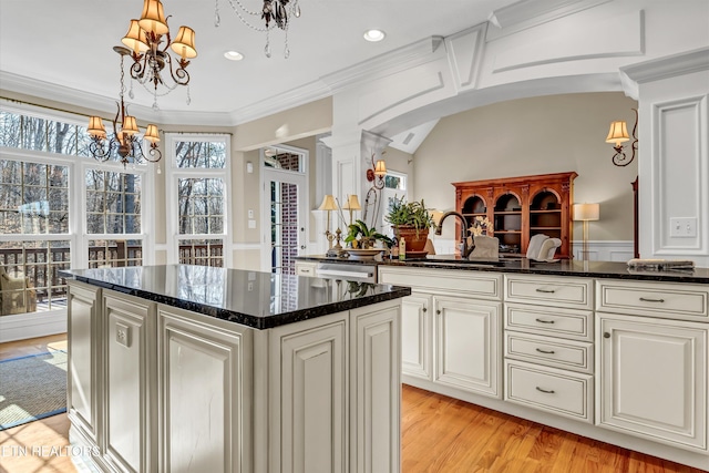 kitchen featuring sink, dark stone countertops, a center island, a notable chandelier, and light wood-type flooring