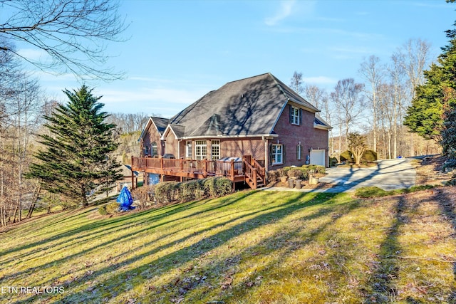 back of property featuring a garage, a wooden deck, and a lawn