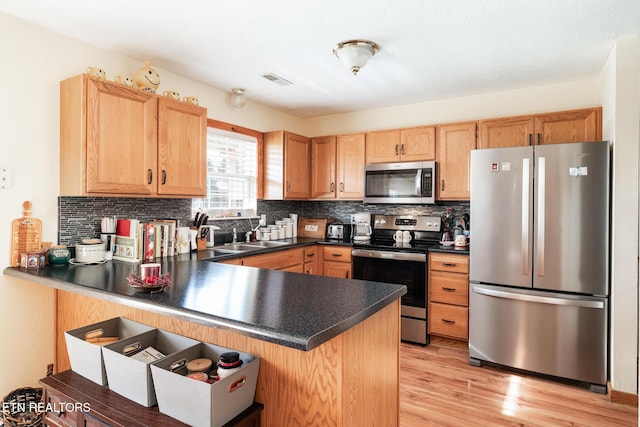 kitchen with sink, light wood-type flooring, kitchen peninsula, stainless steel appliances, and backsplash