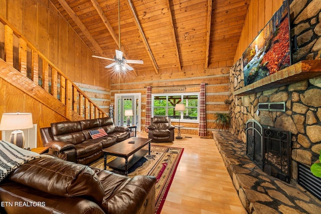 living room with a stone fireplace, wood walls, wooden ceiling, light wood-type flooring, and beam ceiling