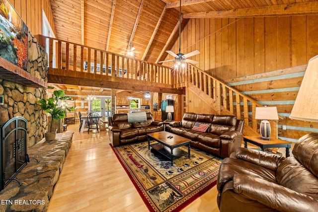 living room featuring a stone fireplace, high vaulted ceiling, wooden walls, wood ceiling, and light hardwood / wood-style floors