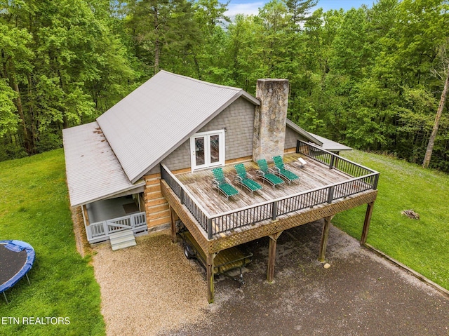 rear view of property featuring a wooden deck, a yard, and a trampoline