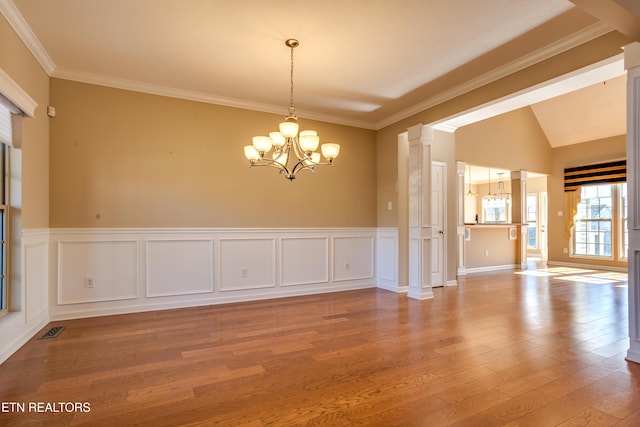 empty room featuring ornate columns, lofted ceiling, a chandelier, hardwood / wood-style flooring, and ornamental molding