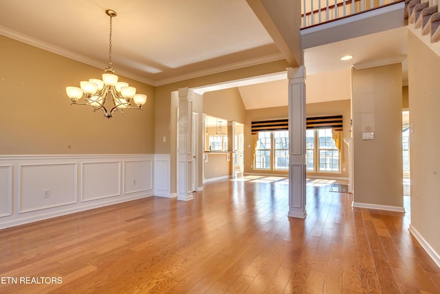 empty room featuring ornamental molding, a chandelier, decorative columns, and hardwood / wood-style floors