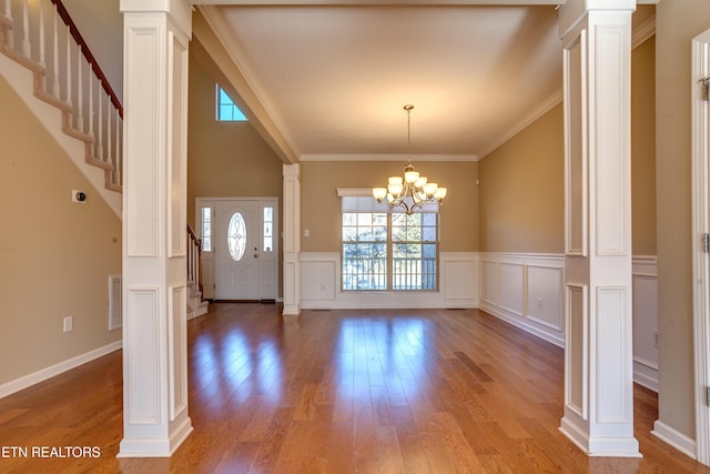 foyer with crown molding, a notable chandelier, wood-type flooring, and ornate columns