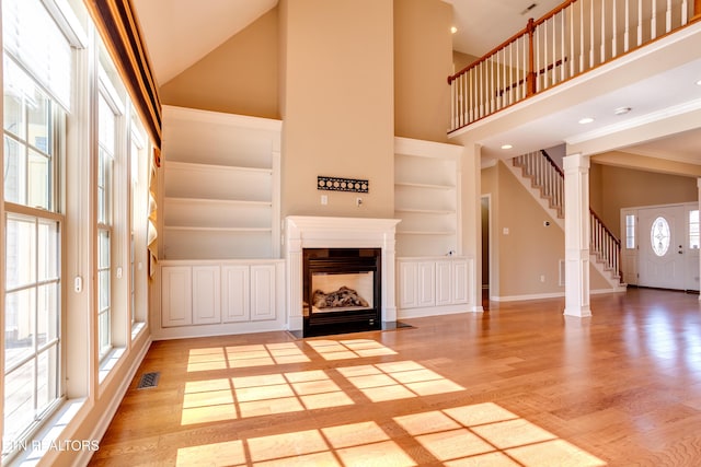 unfurnished living room with built in shelves, a high ceiling, and light wood-type flooring